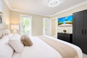 Ein Schlafzimmer mit Bett, Nachttisch, Lampe, Kommode, Fernseher und Tür.