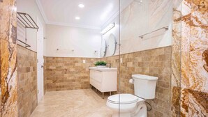 A modern bathroom with a marble backsplash, a white toilet, a glass shower enclosure, and a white vanity with a plant. - Breathtaking 5BR/3BA Villa near Hollywood Beach (Hollywood)