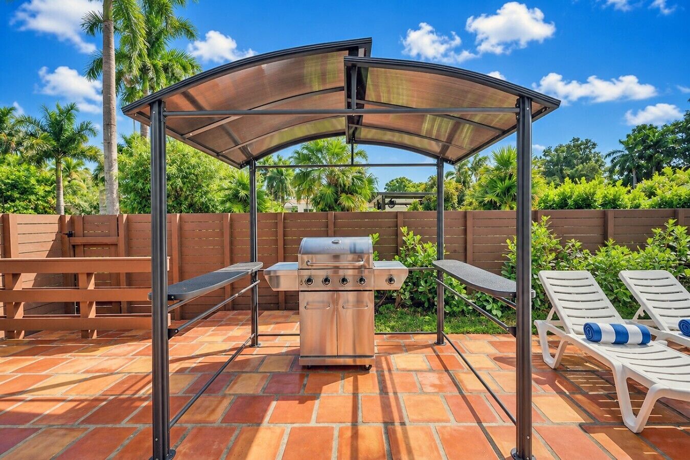 An outdoor barbecue area with a grill, a covered seating area, and lounge chairs.