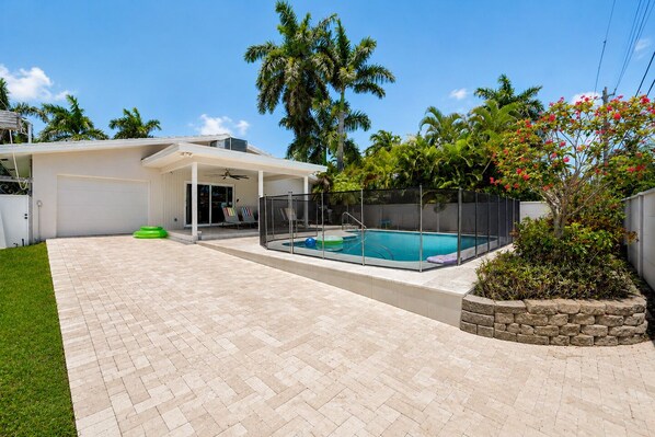 Un patio trasero con piscina, un porche cubierto y un muro de contención de piedra.