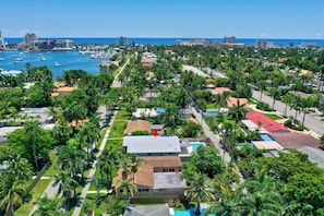 Vista aérea de una zona costera con un puerto deportivo, calles bordeadas de palmeras y edificios con techos rojos.