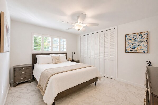A bedroom with a bed, nightstands, a ceiling fan, a window, a closet, and a painting. - WALK TO BEACH 4BR/2BA VILLA IN HOLLYWOOD LAKES (Hollywood)