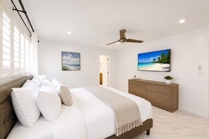 Een slaapkamer met een bed, een plafondventilator, een televisie en uitzicht op het strand.