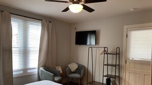 Ein Schlafzimmer mit Bett, Stuhl, Fernseher, Kleiderschrank und Deckenventilator.