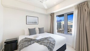 A modern hotel room with a large bed, a ceiling fan, a city view, and a framed picture on the wall.