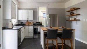A modern kitchen with white cabinets, a stainless steel refrigerator, and a dining area with a wooden table and chairs. - Bright & Cozy Home | Walkable, Private Yard + WiFi (Seattle)