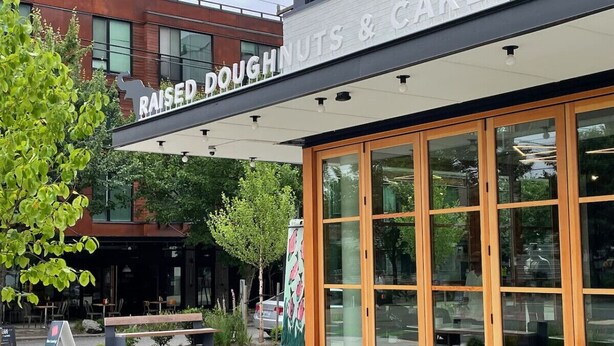 A storefront with large glass windows and a sign reading "Raised Doughnuts & Cakes". - Bright & Cozy Home | Walkable, Private Yard + WiFi (Seattle)