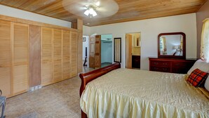 Een slaapkamer met een houten plafond, een bed met een beige sprei, een houten dressoir en een spiegel.