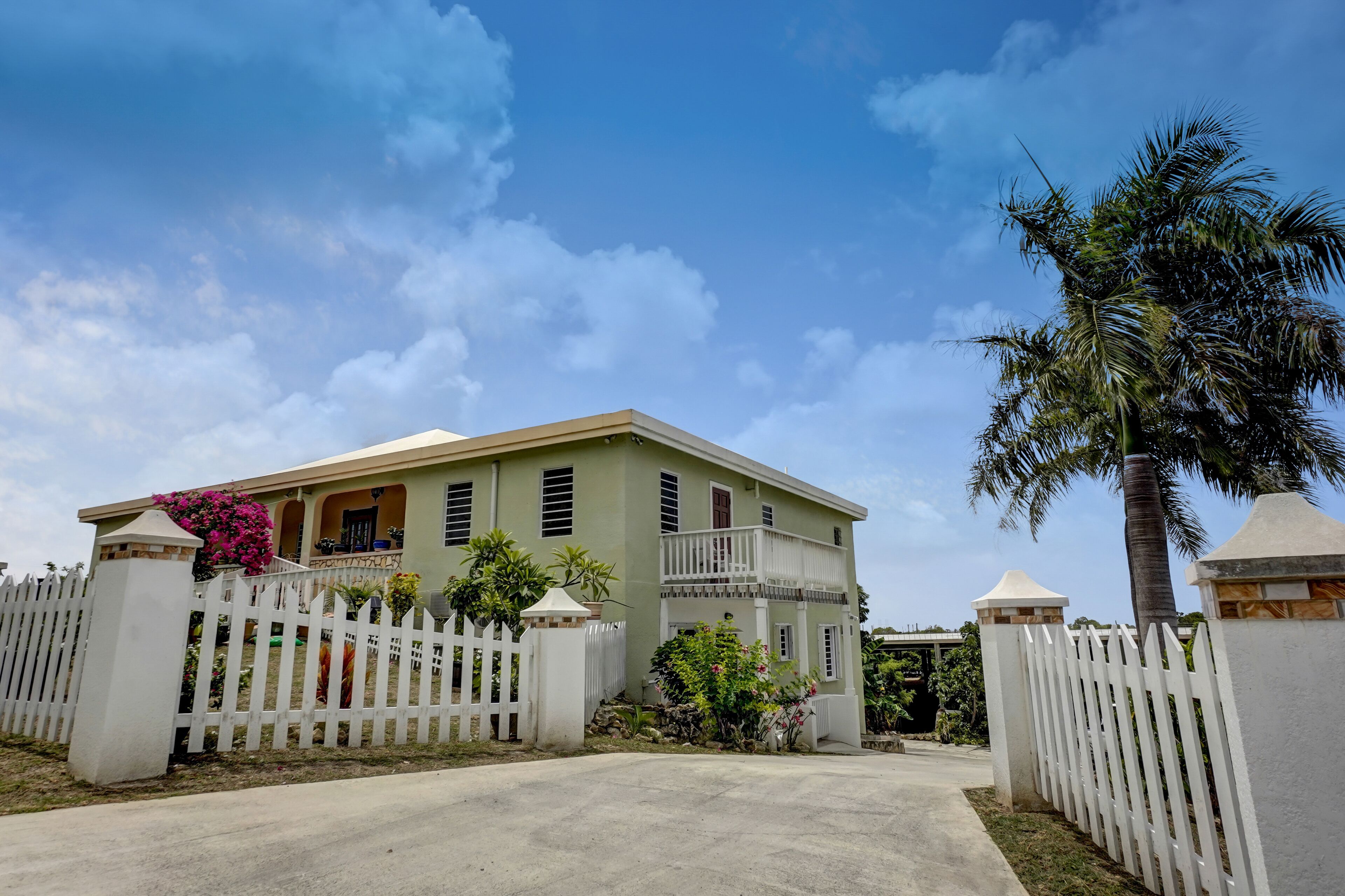 A two-story house with a white picket fence, a balcony, and a palm tree.