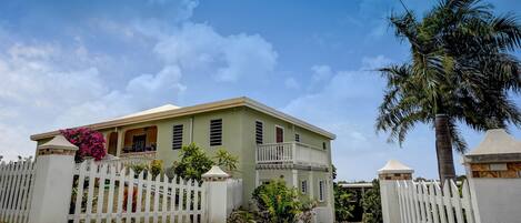 A two-story house with a white picket fence, a balcony, and a palm tree.