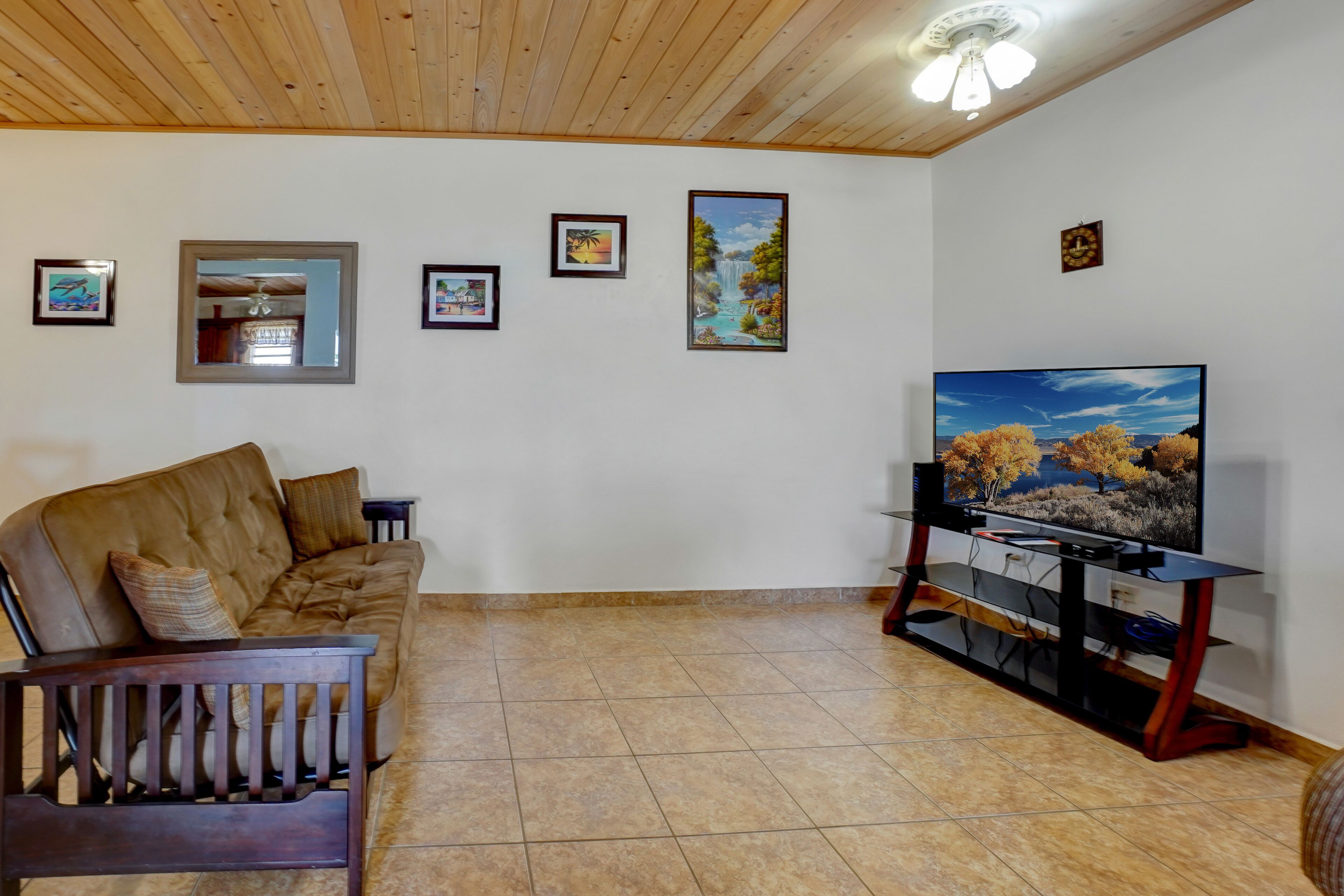 A living room with a brown leather sofa, a television on a wooden stand, and several framed pictures on the wall.