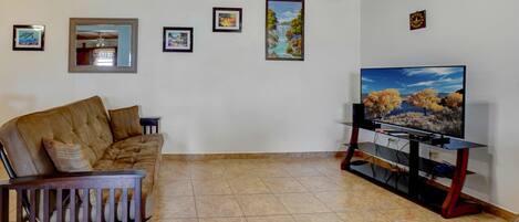 A living room with a brown leather sofa, a television on a wooden stand, and several framed pictures on the wall.