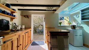 A narrow kitchen with wooden cabinets, a stone wall, and a view through a door to an outdoor area.