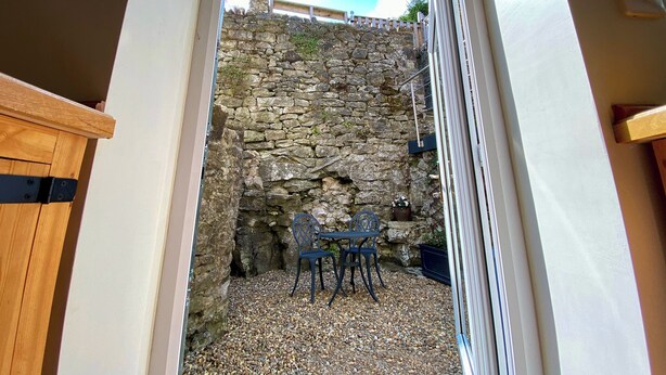A stone wall with a wooden bench and a table, a door leading to a patio area with gravel, and a white wall with a light switch.