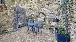 A stone wall with a metal table and chairs in a pebbled area.