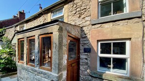 A stone cottage with a wooden front door, a small porch, and a window with a sign reading "TOWMANS COTTAGE 55".