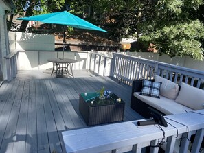 A wooden deck with a table, chairs, a sofa, and a small table with a plant.