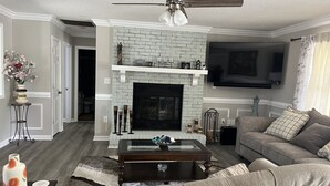 Ein Wohnzimmer mit Kamin, Deckenventilator, Fernseher und einer Couch.