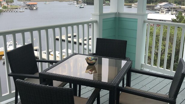 Un espacio al aire libre techado con una mesa y sillas, con vista a un puerto deportivo con barcos y un muelle.