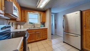 A kitchen with wooden cabinets, a stainless steel refrigerator, a double oven, and a window with blinds.