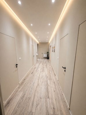 A hallway with wooden flooring, white walls, and doors on both sides. - Joan Luxury Villa Apt with private pool & Gym (Tirana)