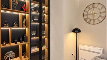 A modern room with a built-in shelving unit displaying various decorative items and glasses, a round wall clock, and a standing floor lamp.