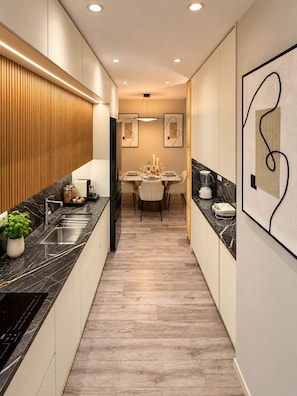 A modern kitchen with a central island, wooden paneling, and a dining area with a chandelier. - Joan Luxury Villa Apt with private pool & Gym (Tirana)