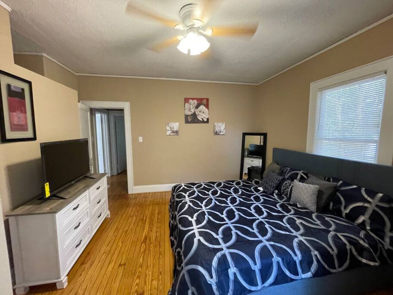 A bedroom with a bed, a dresser, a television, and a ceiling fan.