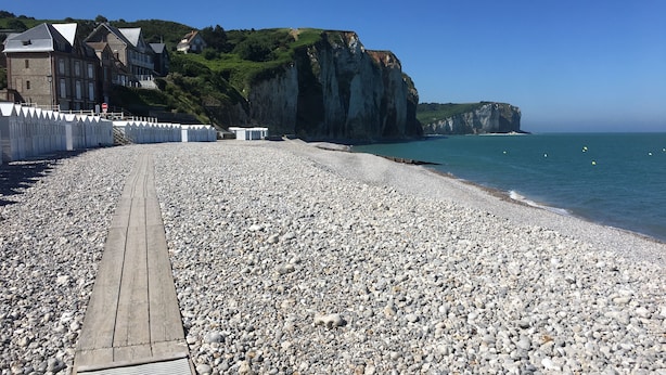 En stenstrand med en træpromenade, der fører hen til en klippe med bygninger.
