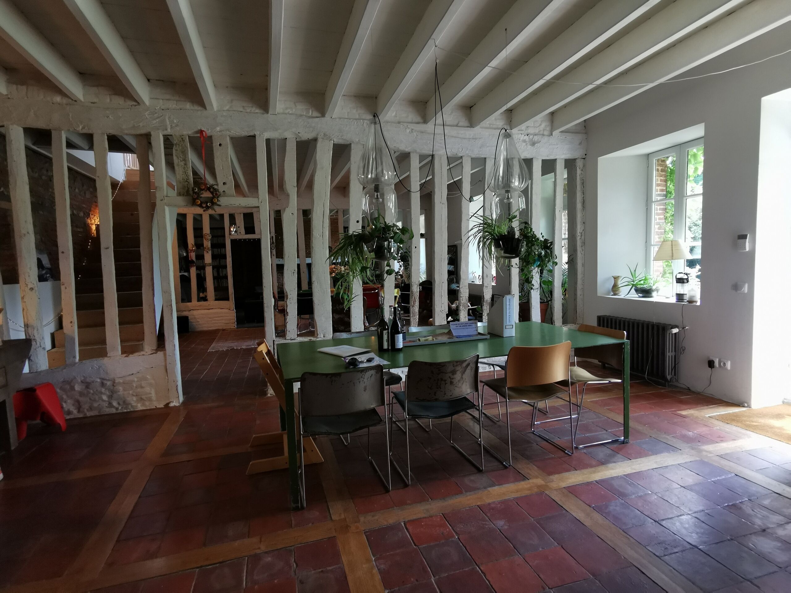 Un comedor con una mesa verde, cuatro sillas, plantas colgantes y vistas a una escalera de ladrillo.