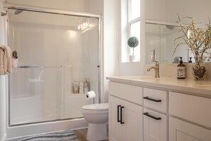 A bathroom with a glass shower enclosure, a toilet, a sink with a mirror, and a potted plant.