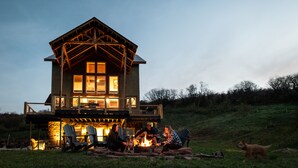 Ein zweistöckiges Holzhaus mit einer Terrasse, einer Feuerstelle und einem Hund in der Nähe.