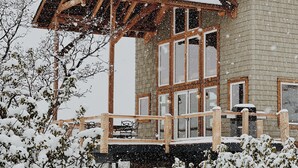 Eine Holzhütte mit Balkon und großen Fenstern, umgeben von schneebedeckter Vegetation.