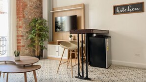 Moderni keittiö, jossa on tiiliseinä, puinen pöytä, kaksi baarituolia, jääkaappi ja seinälle asennettu televisio, joka on sijoitettu työtason yläpuolelle.