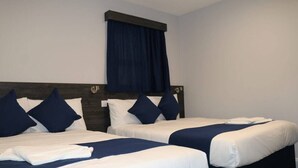 A hotel room with two single beds, dark wood headboards, white bedding, and a dark blue curtain. - Blue Sapphire Hotel (Ilford)