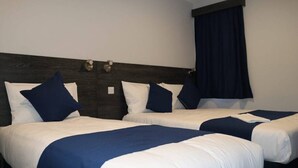 A hotel room with two beds, dark wood headboard, white and blue bedding, and a window with dark curtains. - Blue Sapphire Hotel (Ilford)