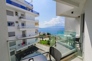 A balcony with a glass table and chair, overlooking a coastal view with buildings and a clear sky. - Dorchester Hotel (Sarandë)