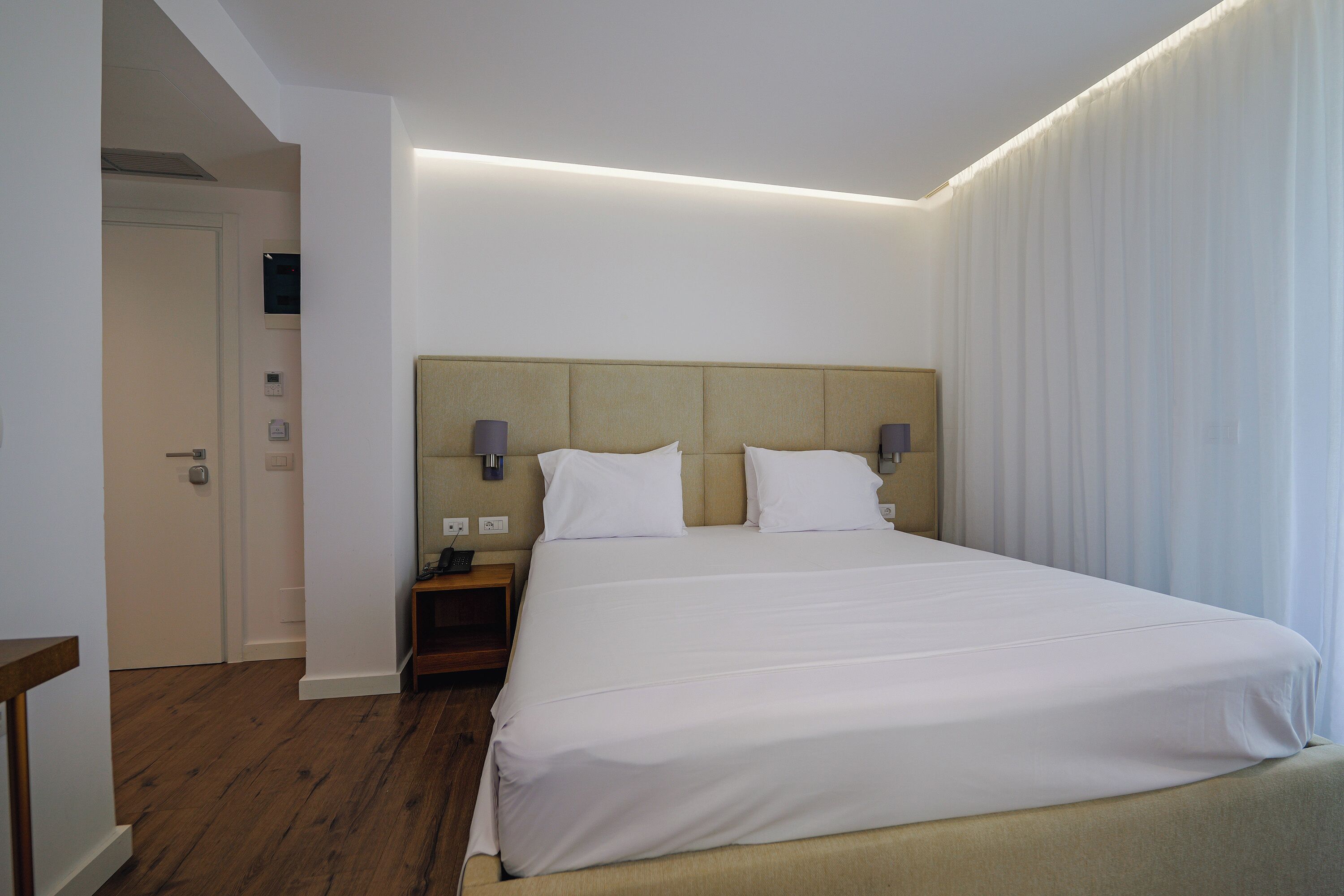 Hotellihuone, jossa on suuri sänky, yöpöydät ja ovi.