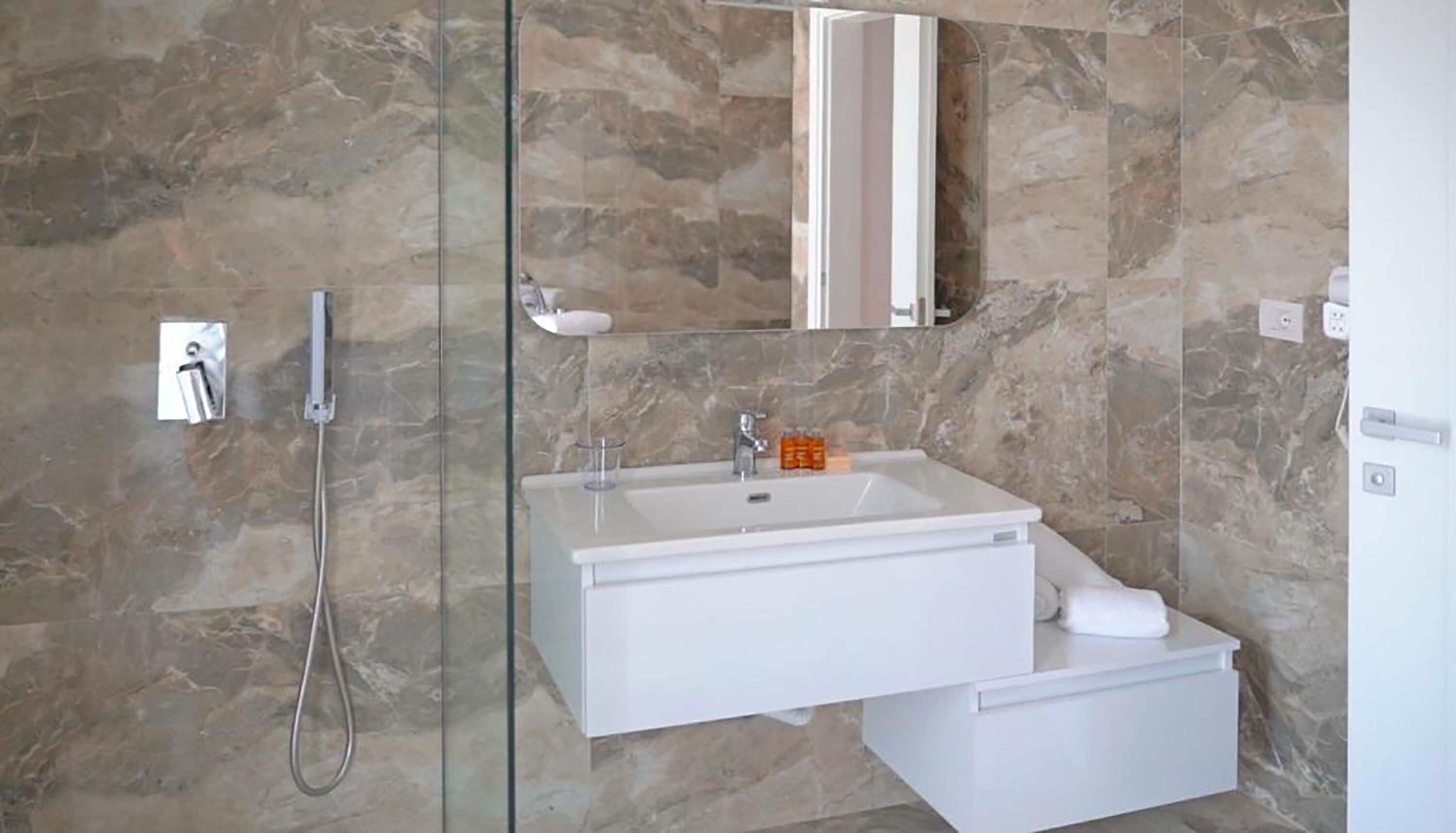 A modern bathroom with a glass shower enclosure, a white sink, and a mirror above it.
