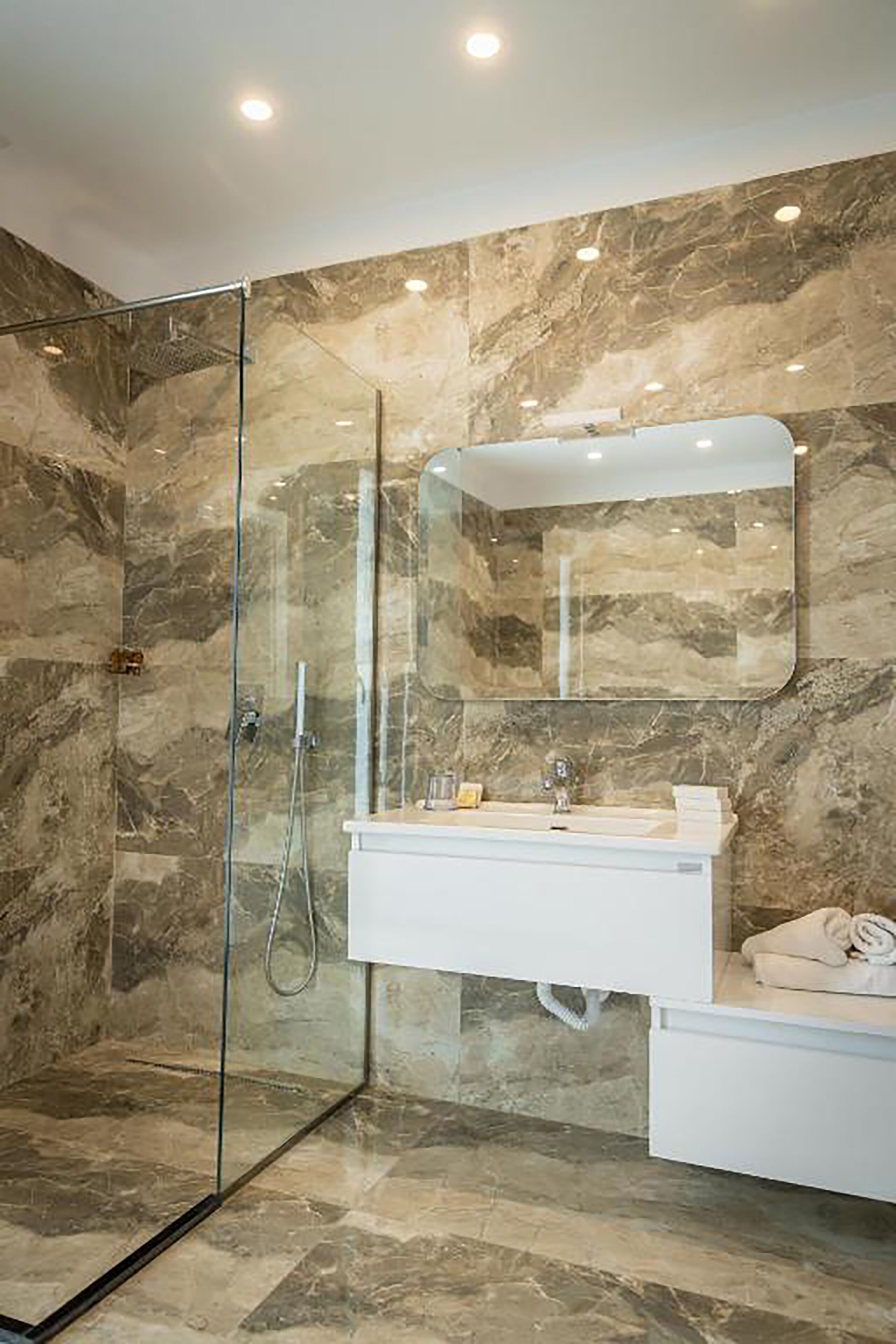 A modern bathroom with a glass-enclosed shower, a white vanity, and marble walls.