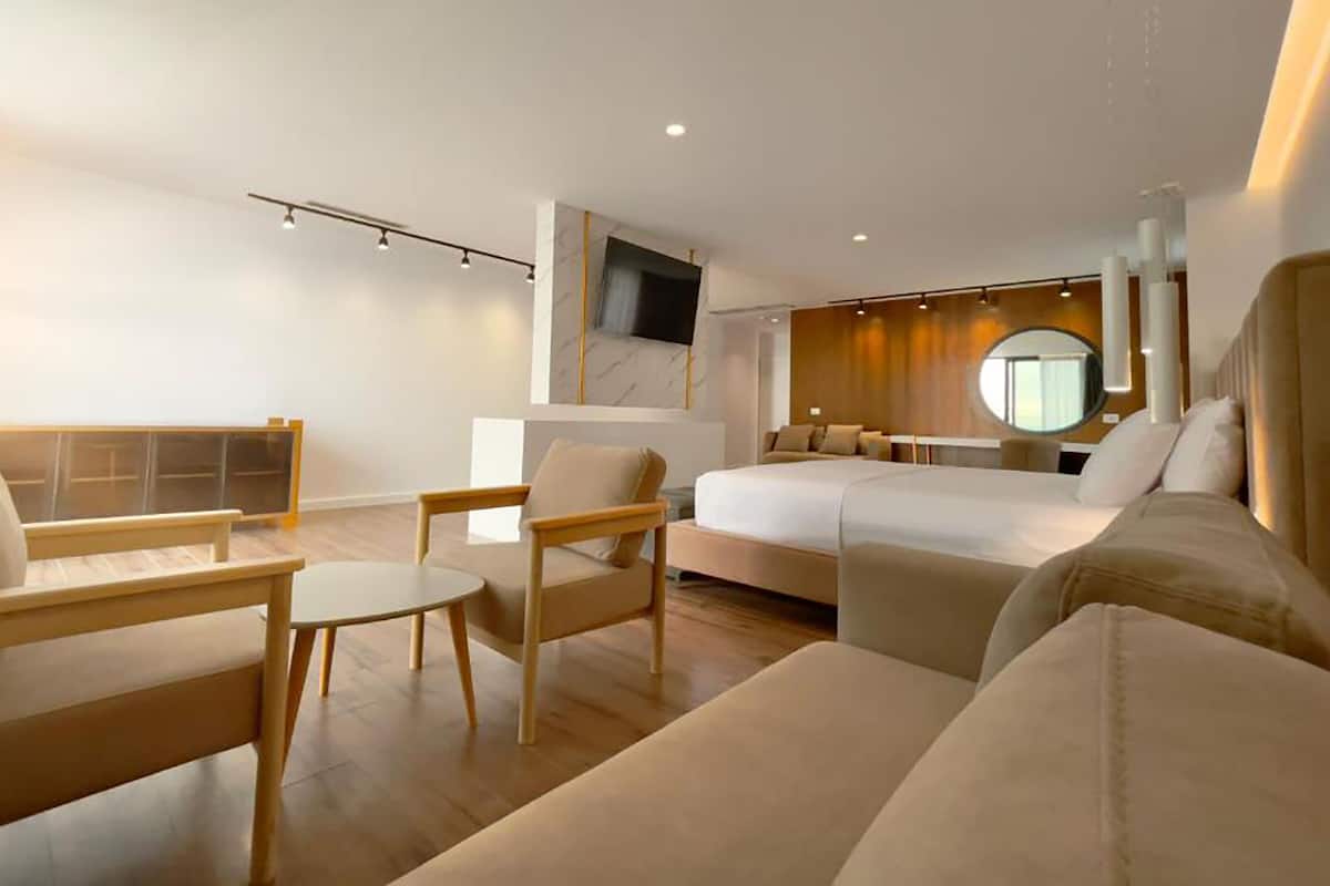 A modern hotel room with a large bed, a seating area with a table, and a TV mounted on the wall.