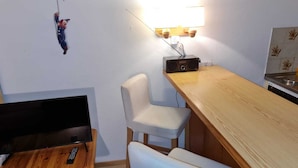 Une petite cuisine moderne avec une table en bois, deux chaises blanches, un téléviseur et une radio.