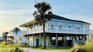 A two-story beachfront house with a balcony, a covered porch, and a staircase leading to the upper level.
