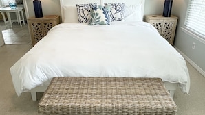A bedroom with a large bed, two nightstands, a bench, and framed artwork on the wall.
