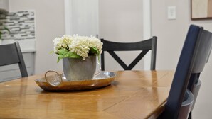 A dining table with a metal pitcher and a saucer, a chair, and a wall-mounted light switch.