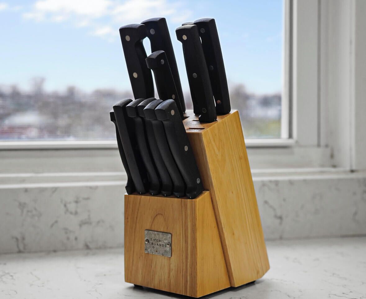 A knife block with multiple knives on a wooden surface near a window.