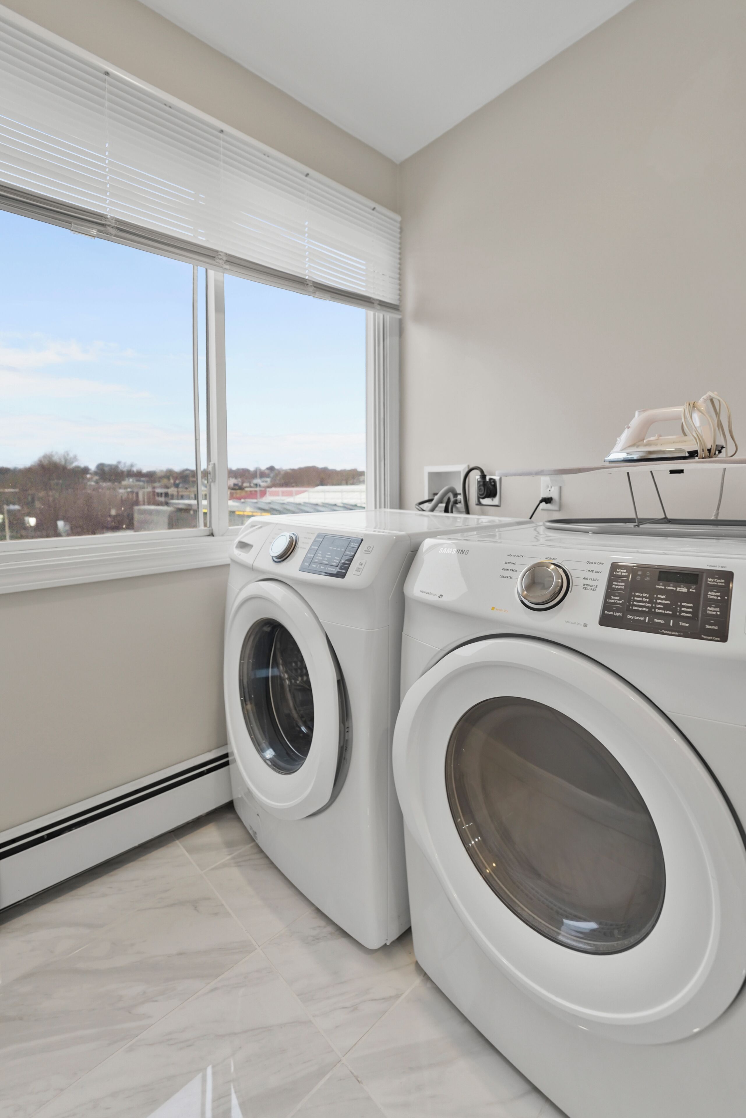 A laundry room with two front-loading washing machines, a dryer, and a window providing a view of the outside.