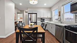 A modern kitchen with stainless steel appliances, a dining area with a wooden table and chairs, and a view of the city through large windows.