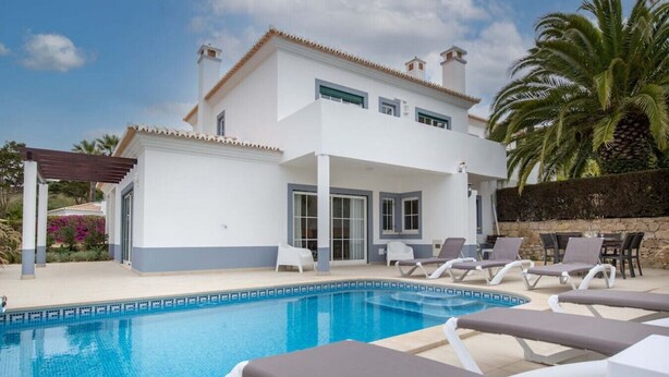 Ein zweistöckiges weißes Haus mit Pool, Sitzgelegenheiten im Freien und einer Pergola.