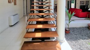 Un interior moderno con una escalera de madera central, un sofá rojo y una planta en maceta en un amplio salón.